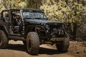 Black Jeep Wrangler Rubicon driving off-road trail with driver waving
